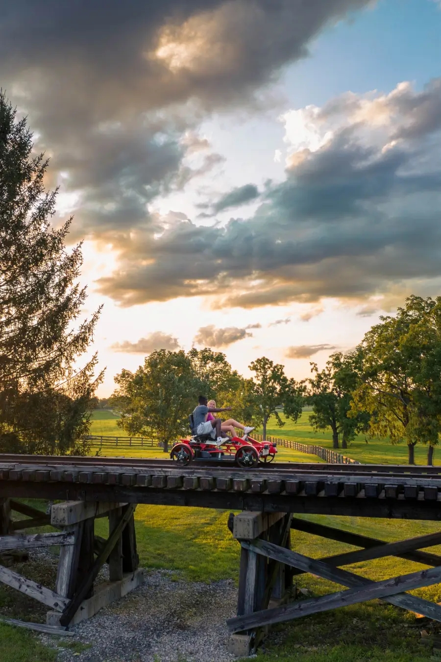A couple crosses over a small bridge with the setting sun in the background.