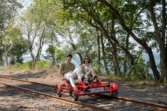 A young couple pedals through the trees alongside the water. 